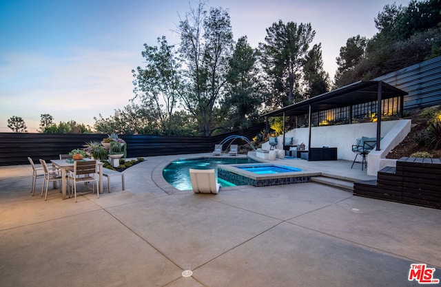 pool at dusk featuring an in ground hot tub and a patio area