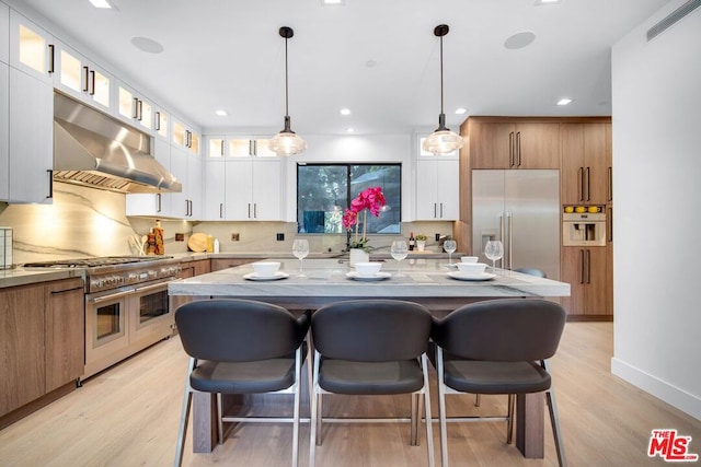 kitchen featuring white cabinets, light stone counters, ventilation hood, high quality appliances, and a kitchen island