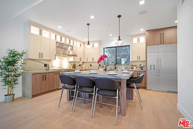 kitchen featuring light wood-type flooring, built in refrigerator, extractor fan, and an island with sink