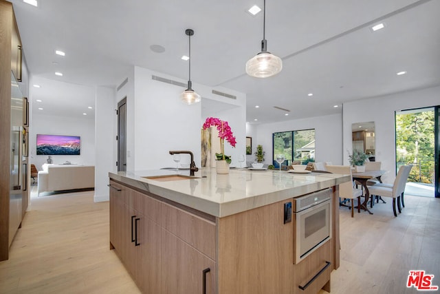 kitchen with sink, light hardwood / wood-style floors, oven, hanging light fixtures, and a large island