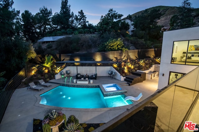 pool at dusk with an in ground hot tub, a mountain view, a patio, and outdoor lounge area