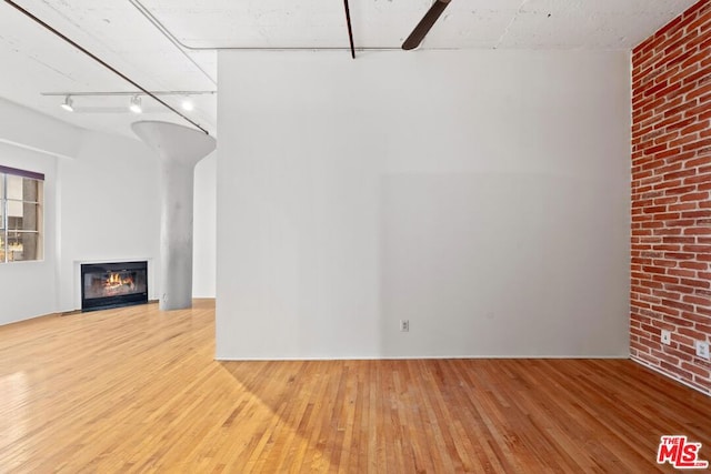 unfurnished living room with hardwood / wood-style floors and brick wall