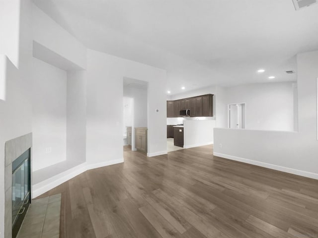 unfurnished living room featuring a tile fireplace and dark hardwood / wood-style flooring