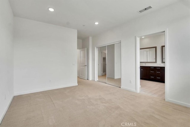 unfurnished bedroom featuring light carpet and ensuite bathroom