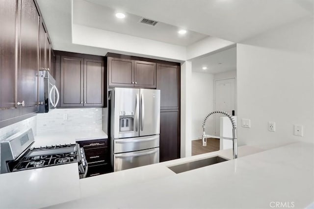 kitchen with sink, kitchen peninsula, decorative backsplash, appliances with stainless steel finishes, and dark brown cabinetry