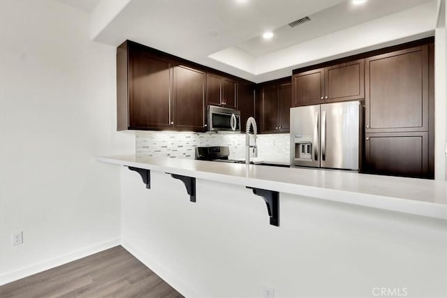 kitchen with dark brown cabinetry, stainless steel appliances, a kitchen breakfast bar, kitchen peninsula, and wood-type flooring