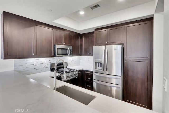 kitchen with appliances with stainless steel finishes, backsplash, dark brown cabinetry, and sink