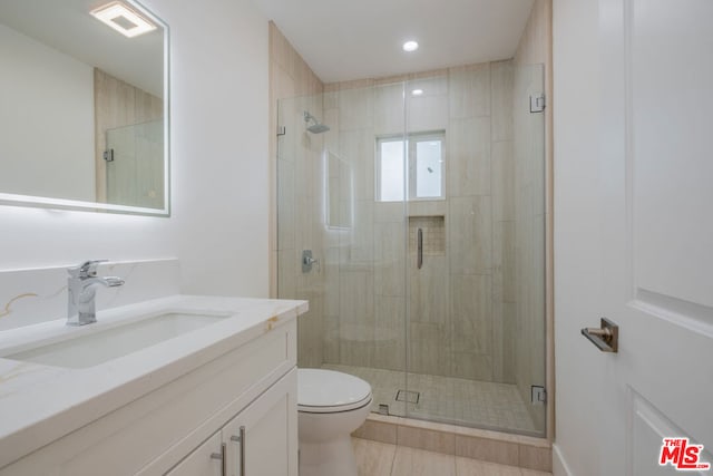 bathroom with tile patterned floors, vanity, a shower with shower door, and toilet