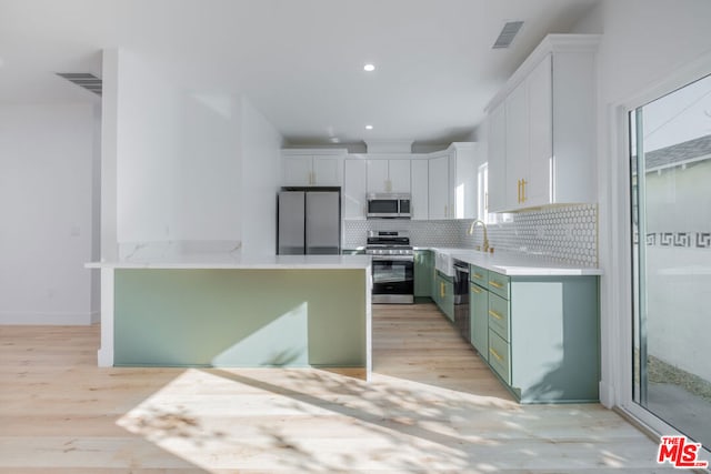 kitchen with white cabinets, green cabinets, light hardwood / wood-style flooring, decorative backsplash, and appliances with stainless steel finishes