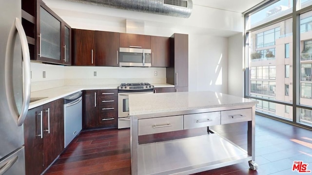 kitchen featuring dark wood-type flooring, light stone countertops, a kitchen island, dark brown cabinetry, and stainless steel appliances