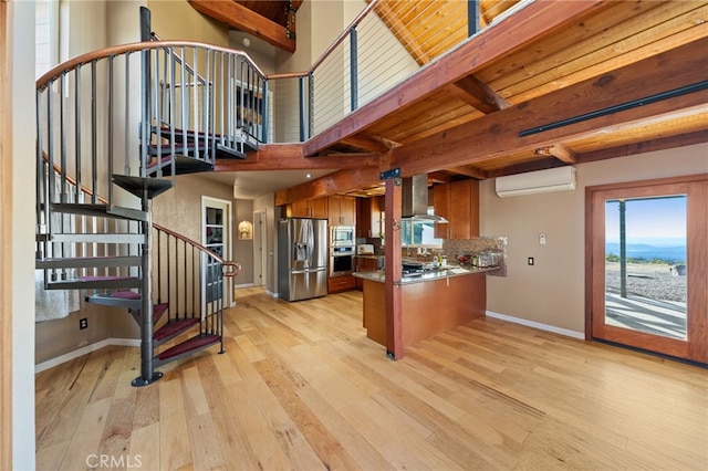 kitchen featuring light hardwood / wood-style flooring, stainless steel appliances, wall chimney range hood, a wall mounted air conditioner, and kitchen peninsula