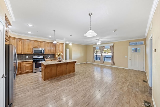 kitchen featuring appliances with stainless steel finishes, light stone countertops, decorative light fixtures, decorative backsplash, and a kitchen island with sink