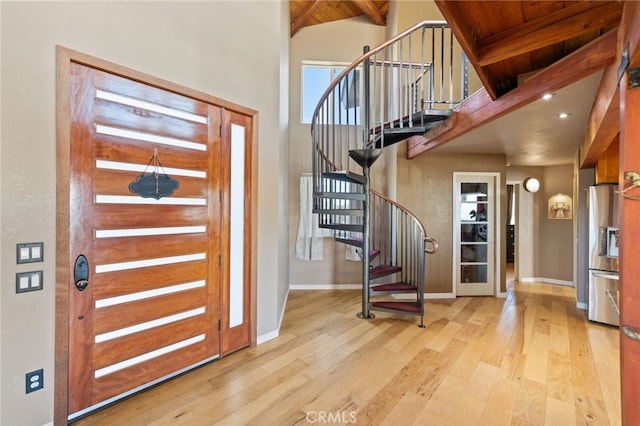 foyer entrance with light wood-type flooring, a towering ceiling, and beam ceiling