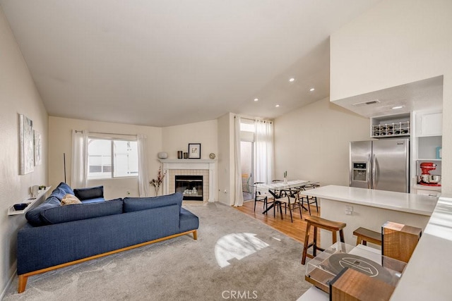 living area featuring recessed lighting, vaulted ceiling, a fireplace, and light wood-style flooring