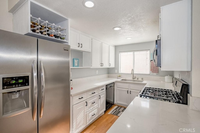 kitchen featuring stainless steel appliances, a textured ceiling, light wood-style floors, white cabinetry, and a sink