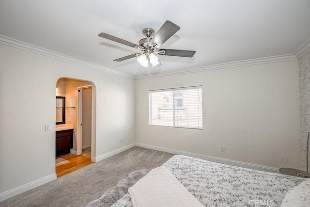 carpeted bedroom with baseboards, arched walkways, ensuite bath, ceiling fan, and crown molding