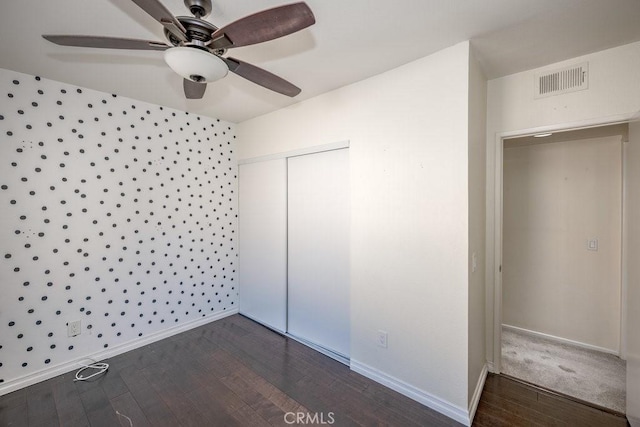 unfurnished bedroom featuring dark wood-style flooring, a closet, visible vents, and baseboards