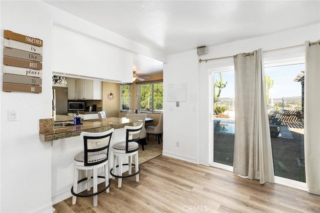 kitchen with ceiling fan, kitchen peninsula, a kitchen bar, white cabinets, and light wood-type flooring