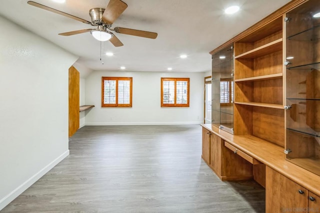 unfurnished living room with built in desk, ceiling fan, and dark wood-type flooring