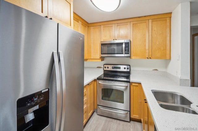 kitchen with light stone countertops, sink, stainless steel appliances, light hardwood / wood-style floors, and light brown cabinetry