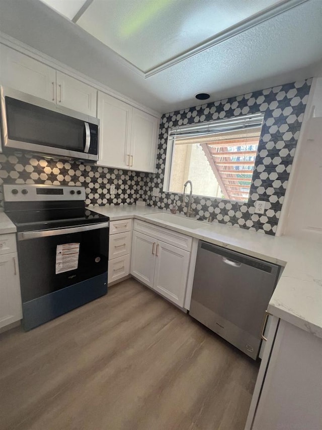 kitchen featuring decorative backsplash, stainless steel appliances, sink, white cabinets, and light hardwood / wood-style floors