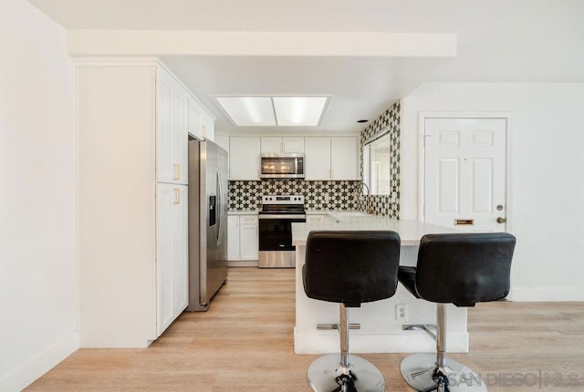 kitchen with kitchen peninsula, a breakfast bar, stainless steel appliances, light hardwood / wood-style flooring, and white cabinets