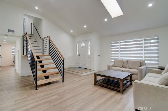 living room featuring a skylight, high vaulted ceiling, and light hardwood / wood-style flooring