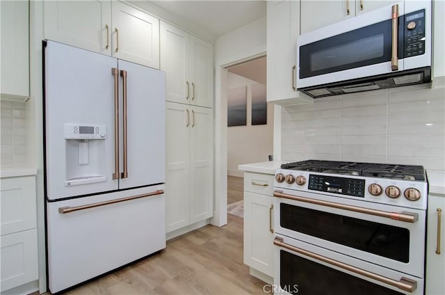 kitchen featuring premium appliances, decorative backsplash, white cabinetry, and light wood-type flooring