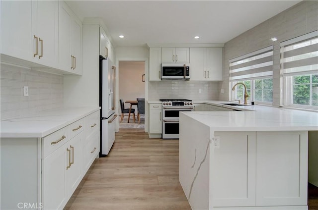 kitchen with white appliances, backsplash, white cabinets, sink, and light wood-type flooring