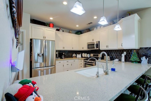 kitchen featuring kitchen peninsula, a breakfast bar, stainless steel appliances, white cabinets, and hanging light fixtures