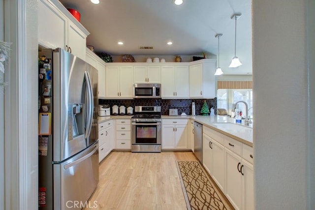 kitchen featuring appliances with stainless steel finishes, sink, decorative light fixtures, white cabinets, and light hardwood / wood-style floors