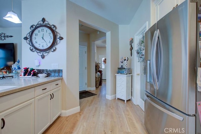 kitchen featuring white cabinets, stainless steel fridge with ice dispenser, light wood-type flooring, and hanging light fixtures