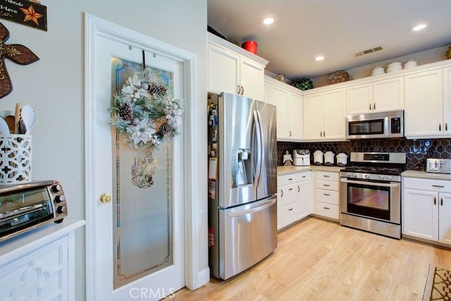 kitchen featuring decorative backsplash, white cabinetry, light hardwood / wood-style floors, and appliances with stainless steel finishes