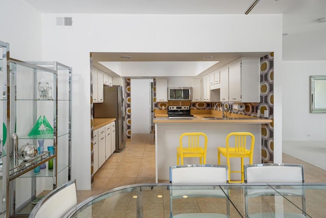 kitchen with kitchen peninsula, stainless steel appliances, sink, white cabinets, and light tile patterned flooring