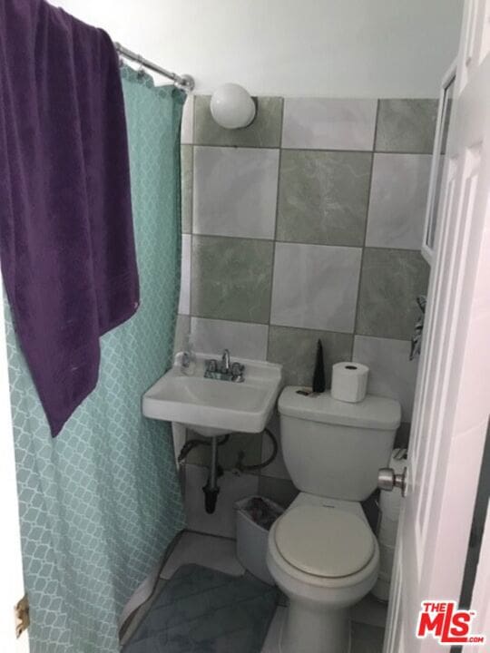 bathroom featuring toilet, curtained shower, sink, and tile walls