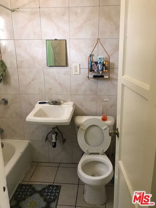 bathroom with tile patterned flooring, a tub to relax in, toilet, and tile walls