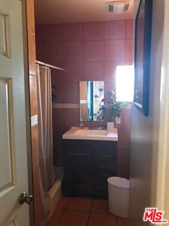 bathroom with vanity, tile patterned floors, tile walls, and shower / tub combo with curtain