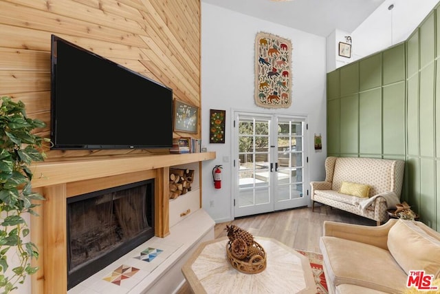 living room with wood walls, french doors, a high ceiling, and light hardwood / wood-style flooring