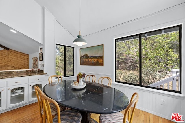 dining space with wood walls, plenty of natural light, vaulted ceiling, and light wood-type flooring