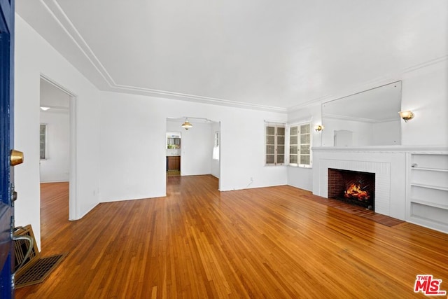 unfurnished living room featuring ceiling fan, hardwood / wood-style floors, ornamental molding, and a brick fireplace