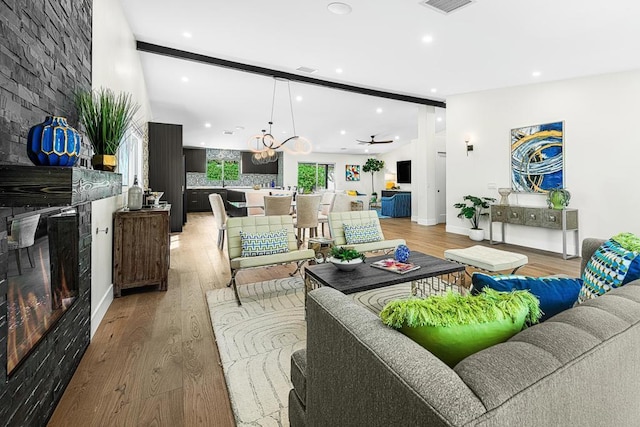 living room featuring beam ceiling, hardwood / wood-style flooring, a stone fireplace, and ceiling fan