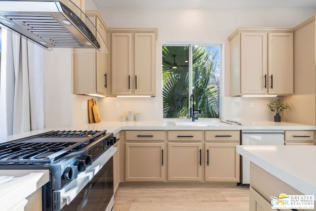 kitchen featuring dishwasher, stainless steel gas range oven, wall chimney range hood, sink, and light hardwood / wood-style flooring