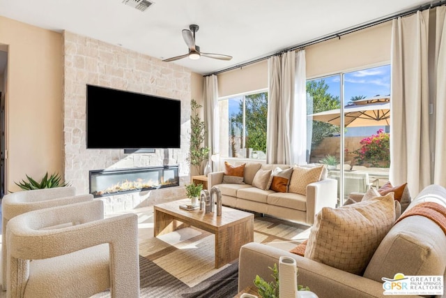 living room with hardwood / wood-style flooring, ceiling fan, and a stone fireplace