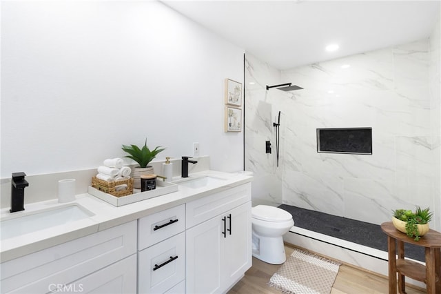 bathroom featuring toilet, wood-type flooring, vanity, and a tile shower