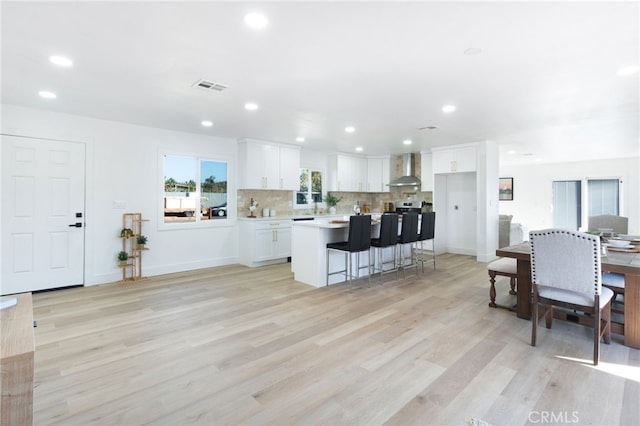 kitchen featuring a kitchen bar, a kitchen island, wall chimney range hood, light hardwood / wood-style floors, and white cabinetry