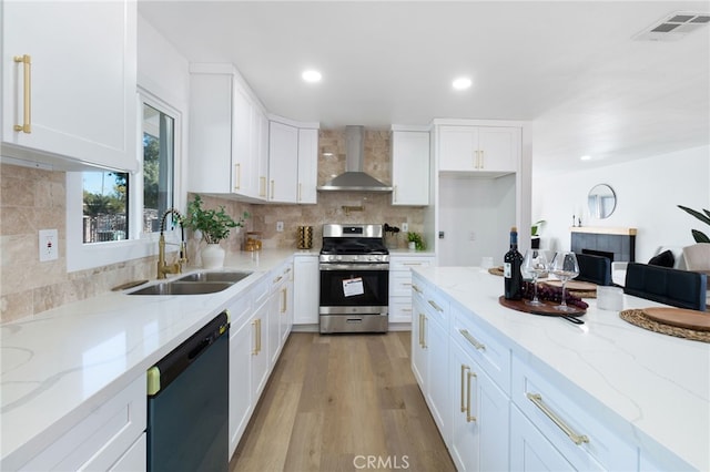 kitchen with light stone counters, wall chimney exhaust hood, dishwashing machine, white cabinets, and stainless steel range with gas stovetop