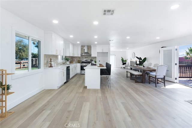 kitchen with dishwasher, white cabinets, light wood-type flooring, a kitchen island, and stainless steel range oven