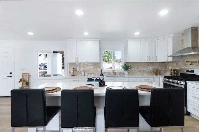 kitchen featuring white cabinets, wall chimney range hood, sink, light wood-type flooring, and a kitchen island