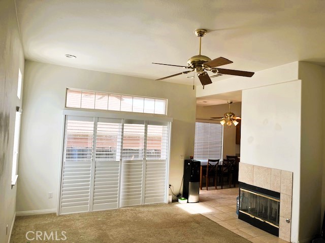 unfurnished living room featuring ceiling fan, light colored carpet, and a tiled fireplace