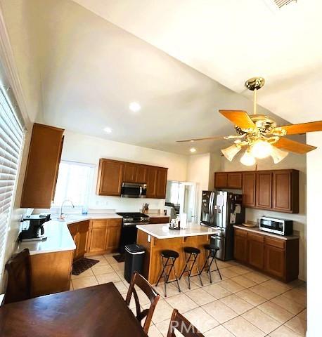 kitchen featuring ceiling fan, light tile patterned floors, a kitchen breakfast bar, a kitchen island, and appliances with stainless steel finishes